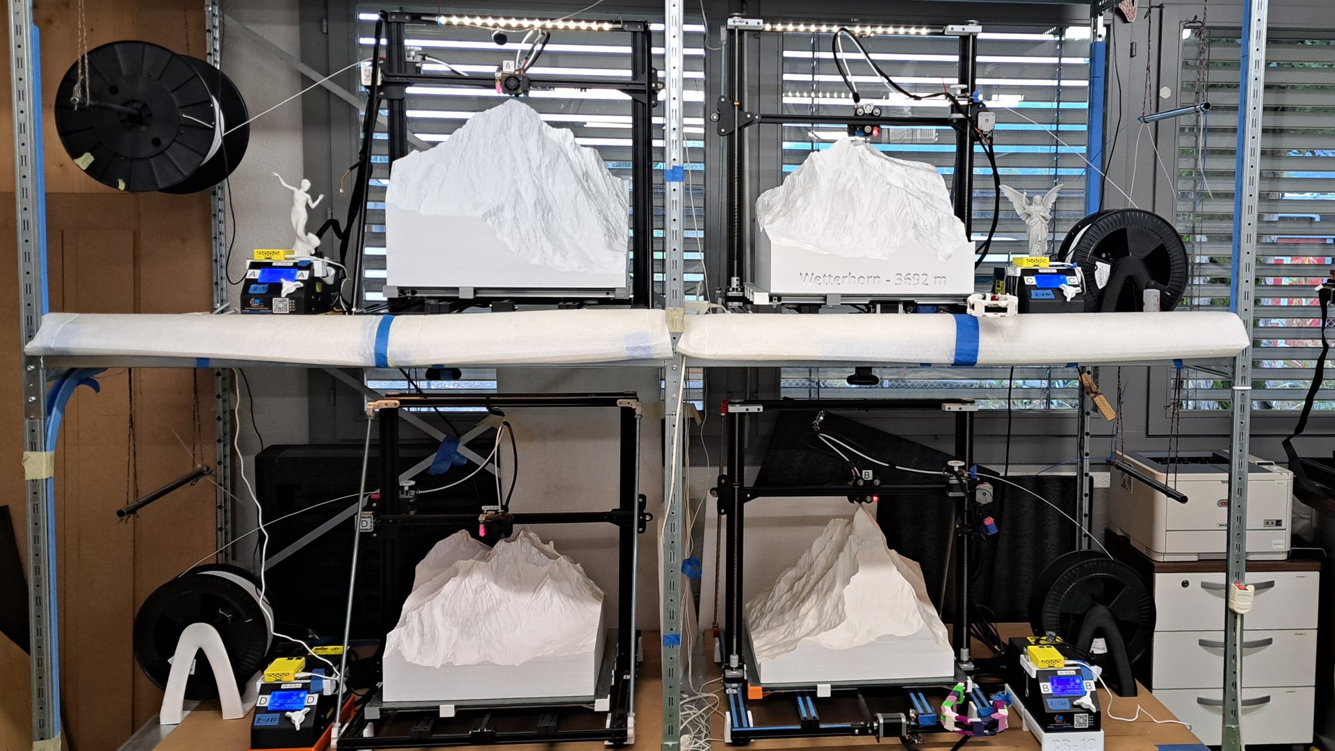 Unsere Werkstatt: vier umgebaute Creality CR-10 S5 mit fertigen Bergreliefs im Regal
